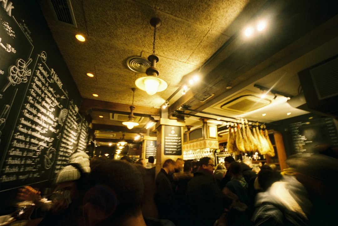 Interior de un bar lleno de gente con jamones colgados y pizarras